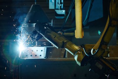 Otomatik kaynak robotu endüstriyel ortamda kesinliğe odaklanan kıvılcımlar yaratıyor. Güçlü mavi ışıklandırma iş başında teknoloji ve makineleri vurguluyor