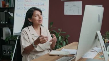 Dil okulunda bilgisayar ekranında oturan İspanyol kadın İngilizce öğretmeninin internet üzerinden video çağrısıyla ders verirken, yeni gramerin çevrimiçi öğrencilere açıklandığı orta boy fotoğraf.