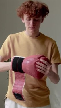 Gündelik giysiler içinde, minimalist odada kırmızı deri boks eldiveni giyen beyaz bir adamın dikey fotoğrafı.