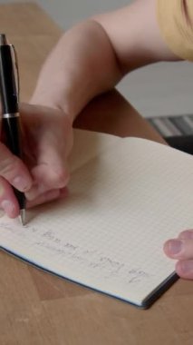 Hardal tişörtlü, ahşap masada oturan ve kalemle deftere mektup ya da kompozisyon yazan kimliği belirsiz bir adamın dikey yüksek açılı görüntüsü.