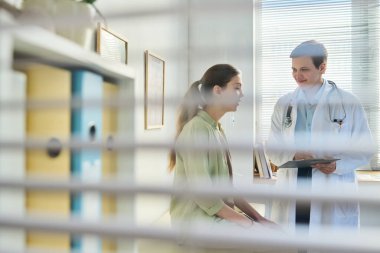 Doktor, genç bayan hastayla sohbet ediyor. Klinik ortamında sağlık bilgilerini tartışırken tıbbi profesyonellerin kullandığı tablet