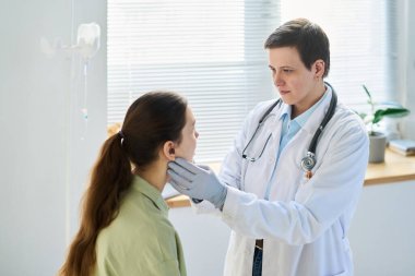 Gündüz vakti klinik ortamda hastaları tıbbi aletle muayene eden doktor doğal ışık dolum odasıyla görüşüyor.