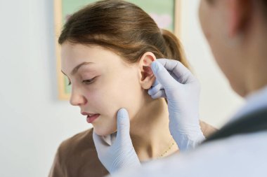 Klinikte kulak kontrolü sırasında hastaların kulağına eldiven takan tıp uzmanı detaylara odaklanıyor. Steril ortamda tıbbi prosedürün yakın çekimi