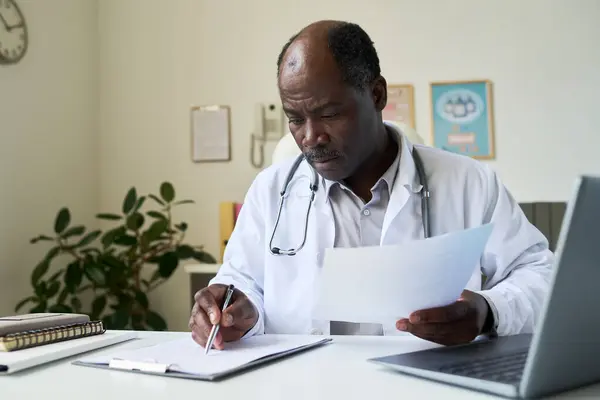 stock image Senior African American doctor reading patient records in modern, well-lit medical office focusing on healthcare management and accuracy enhancing patient care