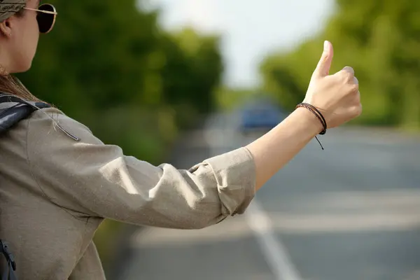 stock image Hand of young woman in grey shirt standing in front of camera by highway and trying to catch car or pickup truck