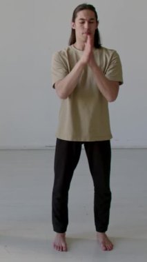 Spor kıyafetleri içinde çıplak ayaklı erkek dansçı stüdyoda durup antrenmandan önce avuç içi ovuyor ve bilek sallıyor.