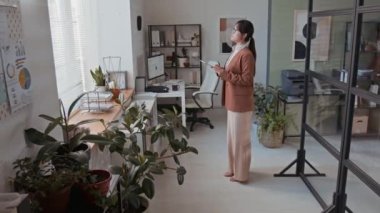 Modern ofiste dijital tablet üzerinde çalışan, yeni iş projeleri geliştiren, şık giyimli ve gözlüklü Asyalı kadın şirket yöneticisinin tam görüntüsü.