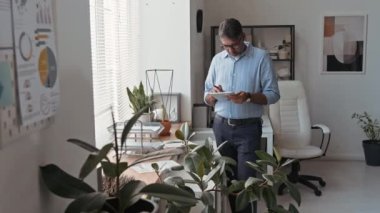 Yeni bir proje üzerinde çalışan ya da modern ofisteki dijital tablet üzerinde iş ortaklarıyla iletişim kuran gözlüklü ve şık giyimli olgun çift ırklı şirket yöneticisinin tam orta ölçekli fotoğrafı.