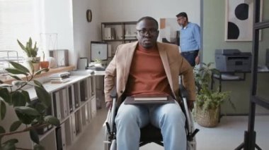 Z jenerasyonunun, gözlüklü ve akıllı gündelik giysileri olan, modern ofiste biyofilik tasarımla tekerlekli sandalyede hareket eden Afro-Amerikan şirket yöneticisinin görüntüsü.