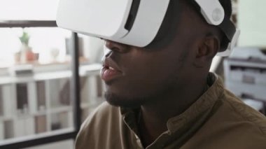 Genç siyahi adamın sanal gerçeklik gözlüklerini takıp, modern ofiste el kol hareketi yaparak iş projesinde çalışmasının yan görüntüsü.
