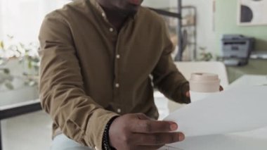 Genç Afro-Amerikan ofis çalışanlarının yakın çekimleri haki gömlekli kahvelerini yudumlarken iş belgelerini modern ofiste analiz ediyorlar.