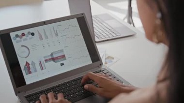 Ofiste çalışırken bilgisayardaki istatistiksel rapor formuna veri yazan kimliği belirsiz kadın yöneticinin omuz üstü fotoğrafı.