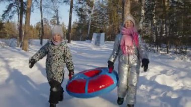Soğuk bir günde, buz gibi bir ormanda kayarak birlikte kış tatilinin tadını çıkardıktan sonra, iki beyaz kızın güvenli bir şekilde kar borusuyla yürümelerini görüntülemek.