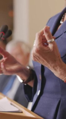 Uluslararası konferansta ya da seçim mitinginde halka hitaben yaptığı konuşmada tribünde duran tanınmayacak kadar olgun kadın politikacının orta boy dikey fotoğrafları.