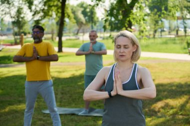 Yetişkin sarışın kadın fitness eğitmeni, kültürler arası erkeklerin önünde dikilirken nefes egzersizi yapıyor.