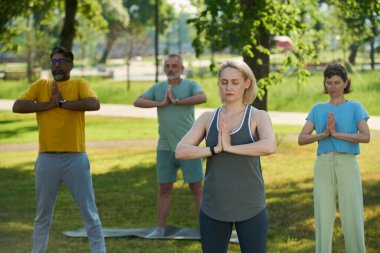 Yetişkin kadın ve erkekler, kadın eğitmenlerin el ele tutuşması üzerine yoga egzersizlerini tekrarlıyorlar.