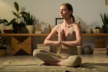 Genç, sakin bir kadın, yerde lotus pozu verirken meditasyon sırasında enerji kaynağını yeniliyor.