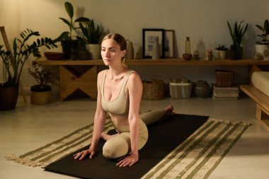 Genç bir kadın bacak esnetme egzersizi yaparken modern iç mekândaki siyah paspasın üzerinde oturuyordu.