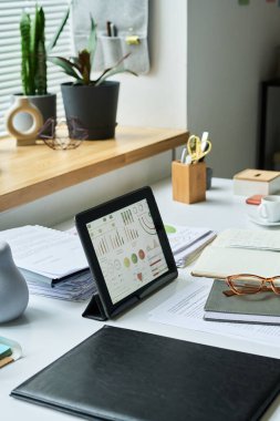 Düzenli bir masada evrak, bitki ve gözlüklerle çevrili dijital tablet, verimliliği ve verimli çalışma alanı yönetimini gösterir