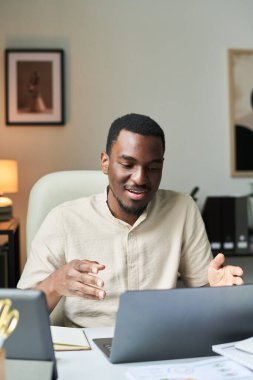 Ofisteki masada oturan gülümseyen adam, dizüstü bilgisayar kullanıyor. Rahat ofis ortamında el ele tutuşurken sohbete dalmak
