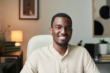 Gülümseyen Afrikalı Amerikalı bir adamın portresi modern ofis ortamında renkli dekorlar ve şık mobilyalarla oturuyor.