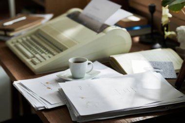 Classic typewriter sitting on wooden desk with stacks of papers and coffee cup. Scene suggests busy writing or office work environment with various documents clipart