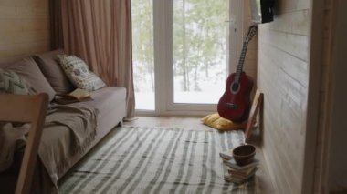 Küçük ve rahat oturma odasının içinde çekilen çekimler yok. Kanepe, halı, gitar, televizyon ve kışın kır evindeki ahşap duvarlarda bulunan soyut çiçek işleri.