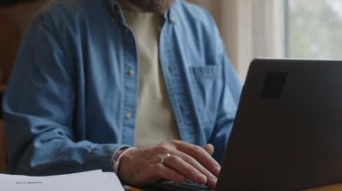 Sakallı Kafkas programcısının laptopta kod yaratıp sıcak kahve içerken görüntüsü. İskandinav tarzı kır evinde uzaktan çalışıyor.