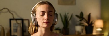 Yoga antrenmanı sırasında kulaklıkla rahatlama müziği dinlerken gözlerini kapalı tutan genç, sakin bir kadının başı.