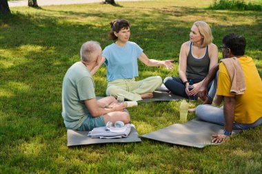 Kültürler arası insanlar arasında mindere oturmuş açık hava yoga eğitiminden bahseden kendinden emin olgun bir kadın.