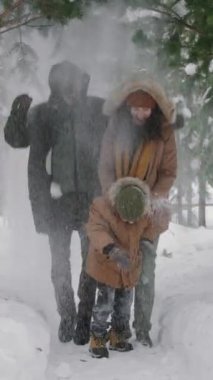 Kış kıyafetleri giymiş, Noel tatillerinde çam ormanlarında kar banyosu yapan, zıplayan ve kahkahalarla gülen genç bir çocukla dolu mutlu bir aile fotoğrafı.
