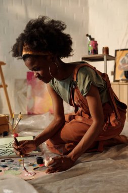 Sanat stüdyosu seti çevredeki resim malzemeleri ve sanat eserlerine odaklanmış kadınların yaratıcı atmosfer sağladığını gösteriyor.