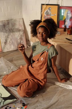 Stüdyoda resim yaparken resim yapan genç bir sanatçı. Etrafında çeşitli sanat malzemeleri ve tuvaller vardı. Doğal ışık büyük pencerelerden sahneyi aydınlatıyor