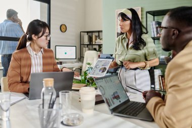 Ofis ortamında proje detayları üzerinde işbirliği yapan takım üyeleri, dizüstü bilgisayarlar ve görsel yardımlar sunum etkisini artırıyor