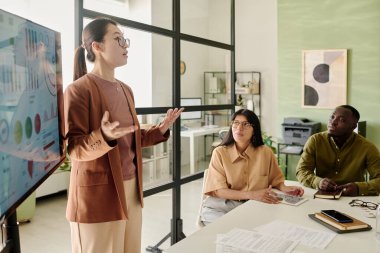 Gündüz toplantılarında teknoloji ve görsel yardımlar kullanarak modern ofis konferans odasında profesyonel sunum bilgileriyle iş verilerini analiz eden çok ırklı bir ekip.