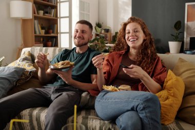 TV 'de ya da ev sinema listesinden film seçerken uzaktan kumandadaki düğmelere basan abur cuburlu neşeli genç kadın.