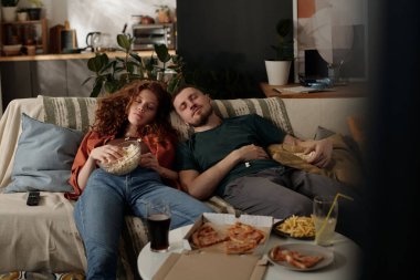 Ellerinde patlamış mısırla genç bir çift evdeki televizyon karşısında rahat bir kanepede kestiriyorlar.
