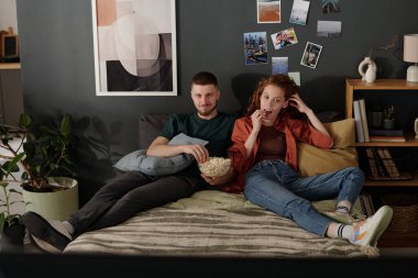 Genç ve dinç bir çift, duvardan duvara oturmuş patlamış mısır yiyor ve TV 'de ya da ev sinemasında film izliyor.