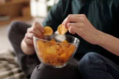Genç bir kadının kaseden kabuklu patates cipsi alıp ev odasında dinlenirken bir erkeğin dizinin üstünde durması.
