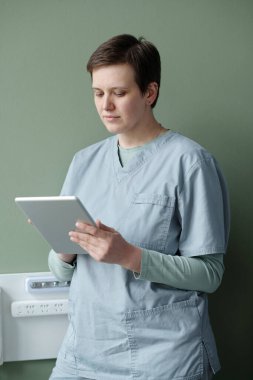 Yeşil bir duvara yaslanıp tıbbi verileri inceleyen ve klinik çevrede çalışan bir tıp uzmanı.