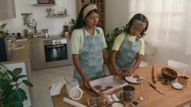 Önlüklü İspanyol anne ve kızı çikolatalı kurabiye pişirirken. Kurabiyeleri tepsiye koyan ve modern mutfakta mini fırına koyan bir kız.