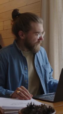 Yeni kitabı üzerinde düşünen sakallı bir yazarın, kış tatilinde İskandinav tarzı kır evindeki ahşap masada dizüstü bilgisayar üzerinde çalışırken orta boy bir resmi.