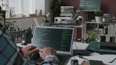Dizüstü bilgisayarda tanımlanamayan erkek programcının orta boy yakın çekim çekimi, siyah ekranda çalışan çizgiler, arka planda tablet üzerinde mobil uygulama projesini tartışan meslektaşlar