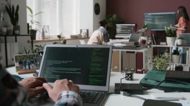 Dizüstü bilgisayardaki anonim erkek yazılım geliştirici kodlama algoritması, siyah ekranda çalışan çizgiler, arka plandaki multimedya ekranında projeyi tartışan erkek ve kadın.