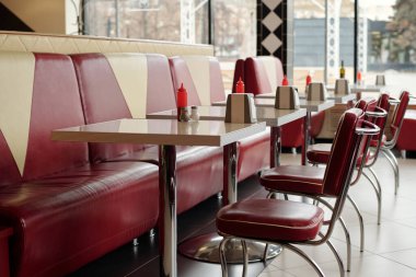 Canlı retro restoran vitrinleri, parlak kırmızı vinil kabinler ve krom masalar. Her bir masayı paslanmaz çelik aksanlar ve çevreyi tamamlayan geometrik duvar kağıtlarıyla donatan konserve dağıtıcıları.