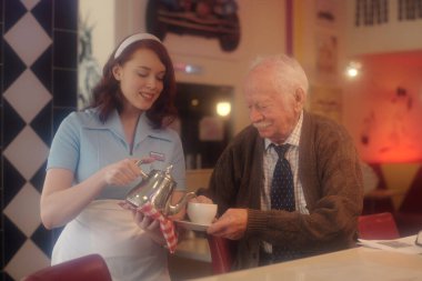 Eski tarz lokantada kıdemli bir adama çay servisi yapan Kafkas garson canlı, nostaljik atmosferde sıcak bir gülümseme paylaşıyor.
