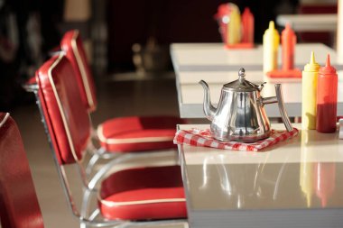 Kırmızı sandalyeler ve kareli peçetenin üzerinde metal kahve demliği ve çeşni şişeleriyle çevrili Retro Dinar ayarları.