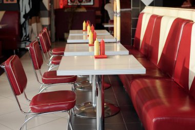 Retro restoranın içi kırmızı deri koltuklar ve her masada baharat şişeleri olan beyaz masalarla dolu, nostaljik bir ortam yaratıyor.