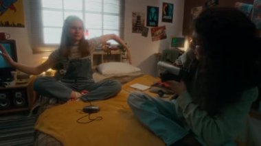 90 'lı yıllarda yatak odasında birlikte takılırken el sallayan ve retro vhs kamerasına dans eden neşeli Y kızını kaydeden gülümseyen kabarık saçlı çocuğun el kamerasıyla tam görüntüsü.