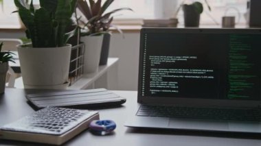 Bilgisayara yakın çekim yapan kimse yok. Programlama kodları ofisteki bilişim mühendisinin masasında derleniyor. Not defteri, tablet, el tutucu, demlik bitkileri, kahve bardağı bitkileri.